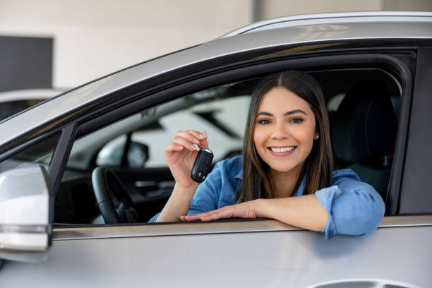 A happy driver holding car keys and smiling next to a modern vehicle
